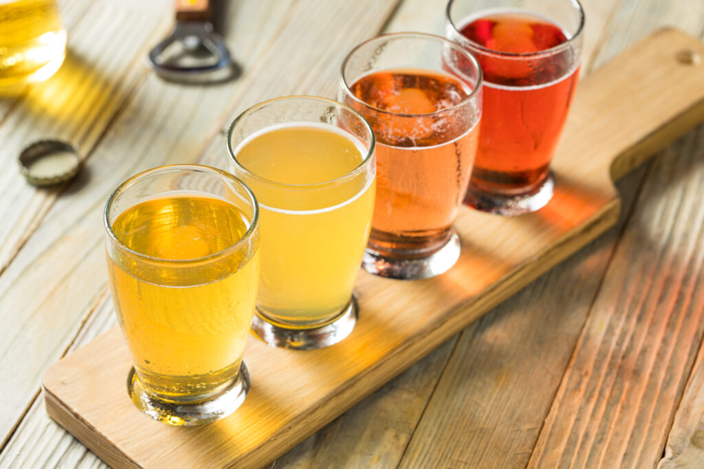 Four glasses of cider in golden and amber colours on a wooden tasting board